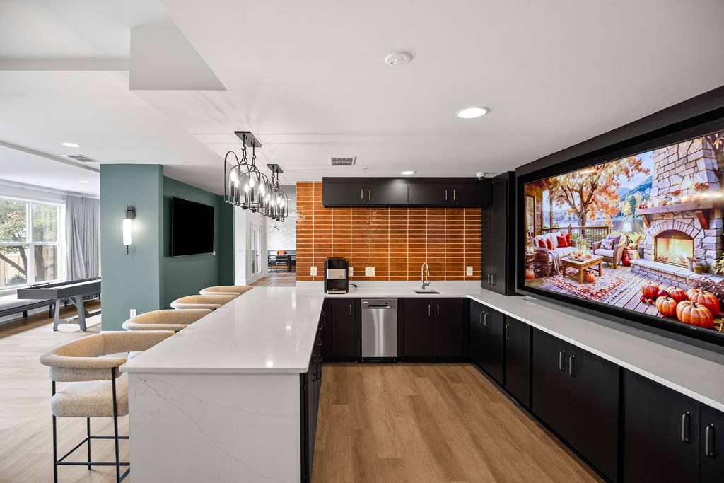 A modern kitchen with a long white island and a large TV mounted on the wall.