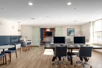 A modern office space with a long table and chairs, computers, and a blue sofa.
