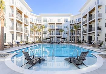 A swimming pool surrounded by lounge chairs in front of apartment buildings.