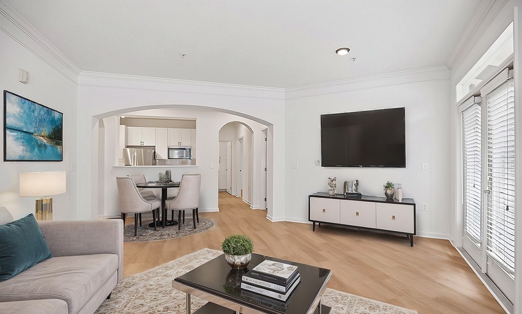 A living room with a grey couch, a coffee table, a dining table, and a television mounted on the wall.