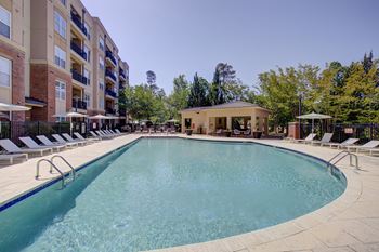 A large outdoor swimming pool surrounded by sun loungers and a building in the background.