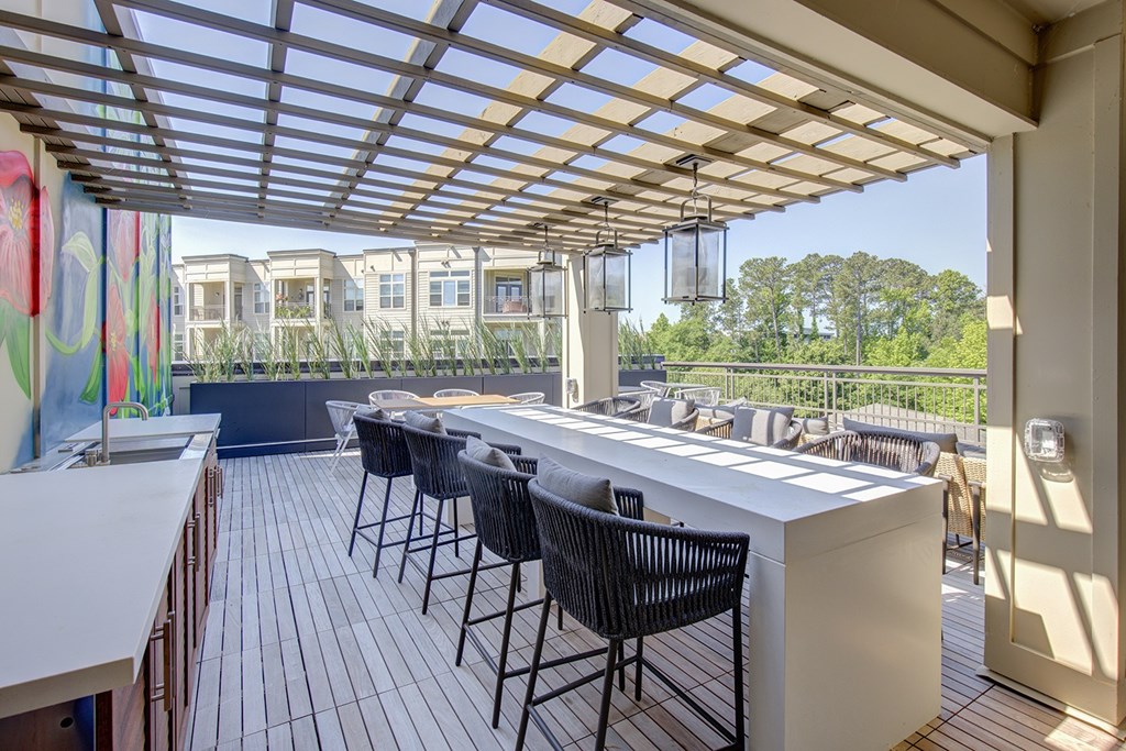 A white bar with black chairs is under a white roof.