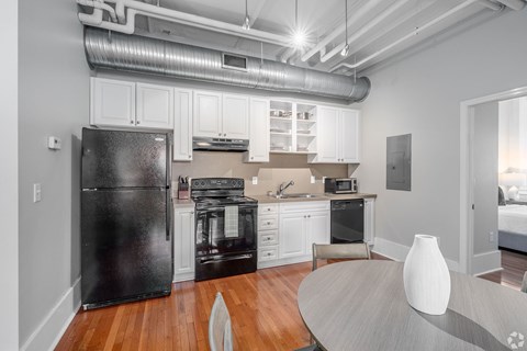 A black refrigerator is in a white kitchen with wooden floors.