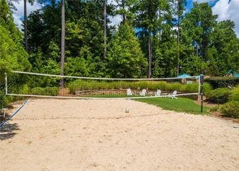 A sandy volleyball court surrounded by trees and a fence.