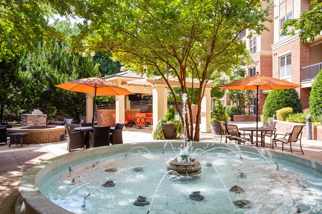 A fountain in the middle of a patio surrounded by chairs and umbrellas.