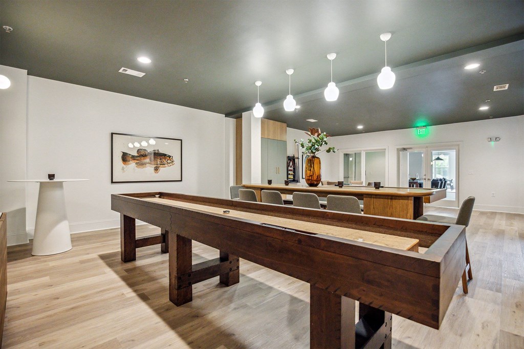 A long wooden table is in the middle of a room with a pool table and a painting on the wall.