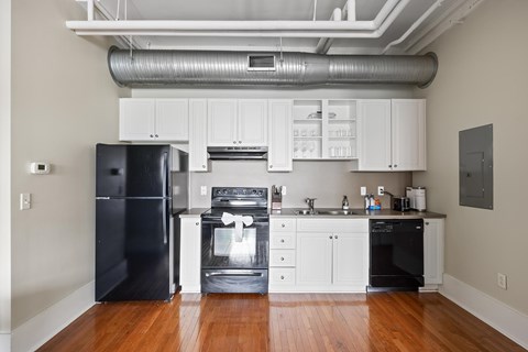 A black refrigerator is in a kitchen with white cabinets.