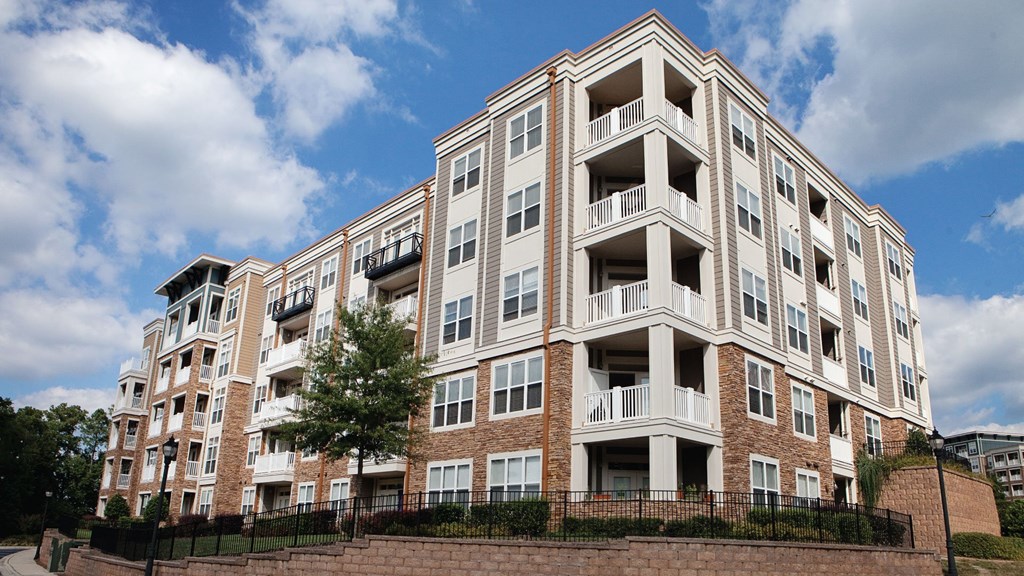 A large apartment building with balconies and a brick wall in front.