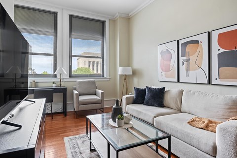 A living room with a grey couch, a glass coffee table, and a painting on the wall.