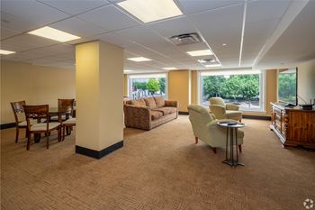 A spacious waiting room with a carpeted floor and a view of trees outside the window.
