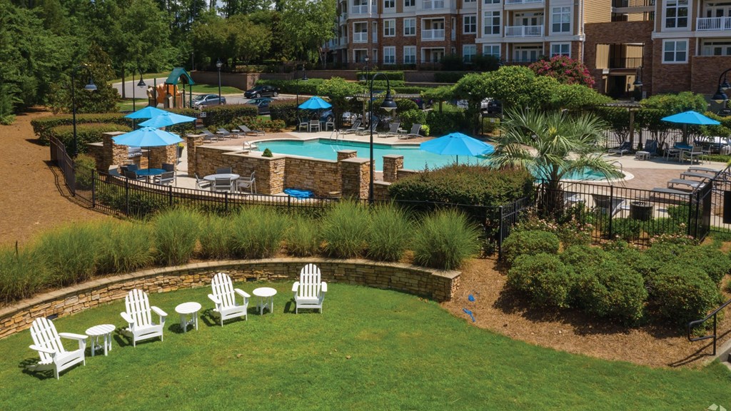 A pool surrounded by a grassy area with chairs and umbrellas.