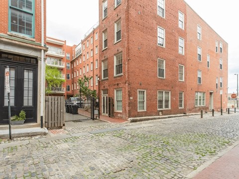 A cobblestone street leads to a red brick building.