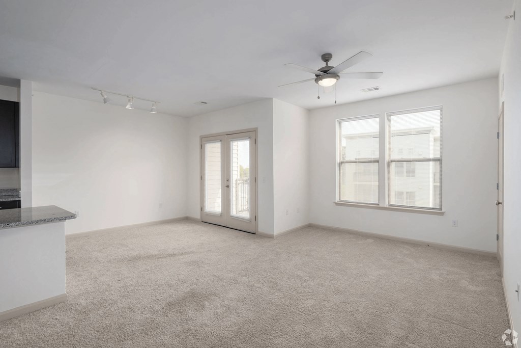 A spacious living room with a ceiling fan and carpeted floor.