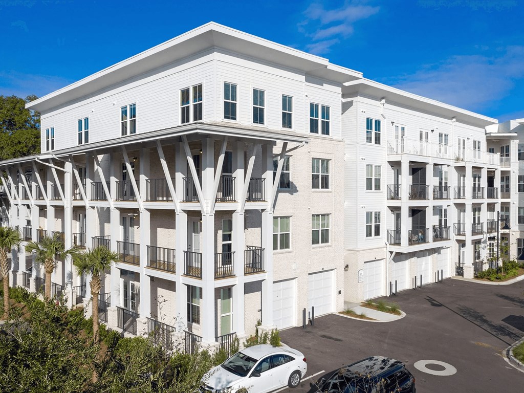 A white building with balconies and a car parked in front.