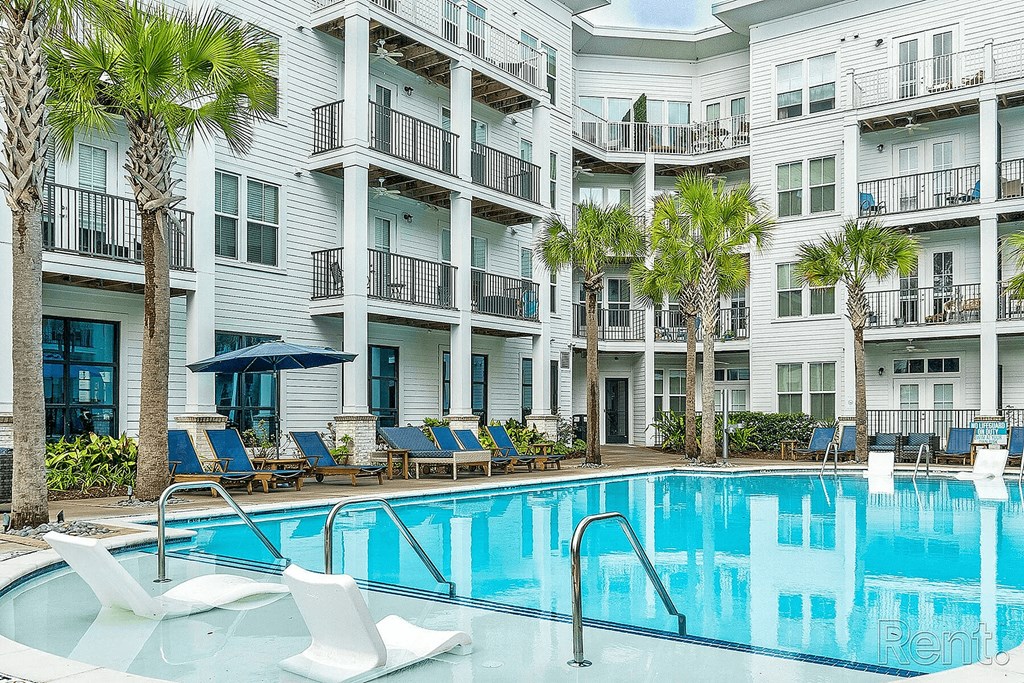 A swimming pool with lounge chairs and palm trees in front of a white apartment building.