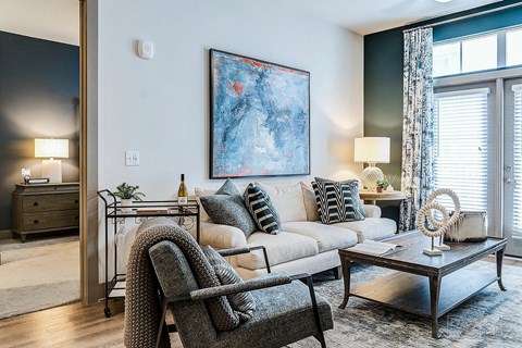 A modern living room with a grey chair, a white sofa, and a large painting on the wall.