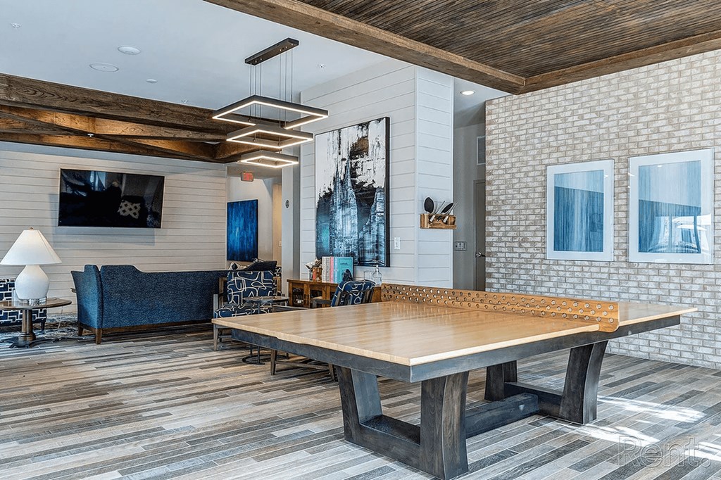 A large wooden table is in the middle of a room with a blue couch and a television mounted on the wall.
