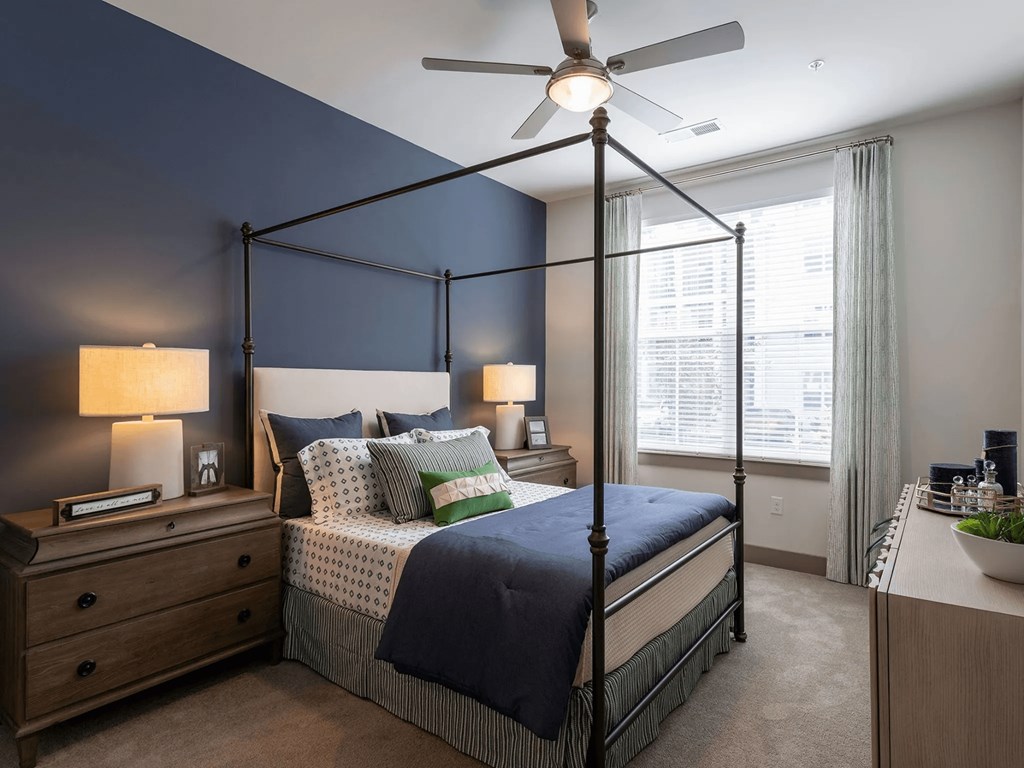 A bedroom with a four-poster bed, a ceiling fan, and a nightstand with a lamp.