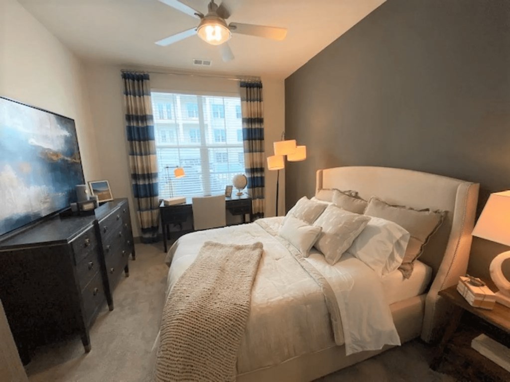 A bedroom with a large bed, a television, and a window with curtains.