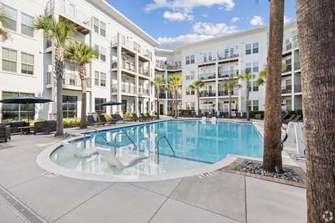 A large swimming pool is surrounded by palm trees and lounge chairs.