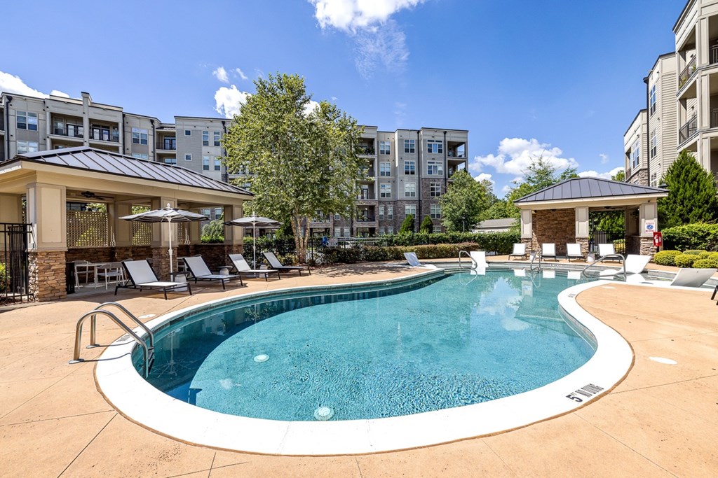 A large swimming pool surrounded by lounge chairs and umbrellas in a sunny day.