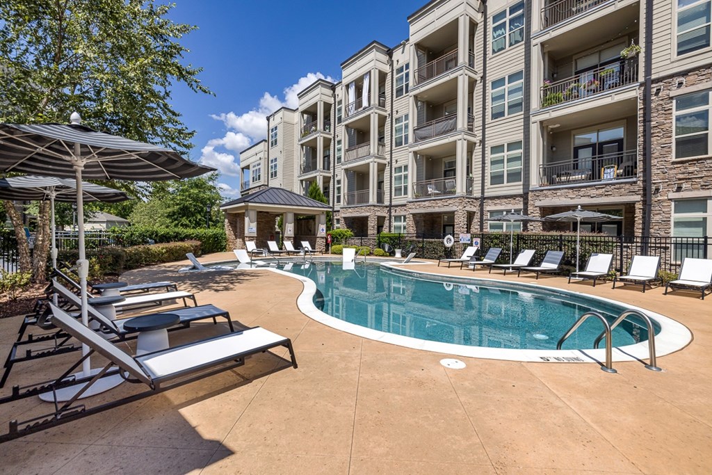 A swimming pool surrounded by lounge chairs and umbrellas in front of apartment buildings.