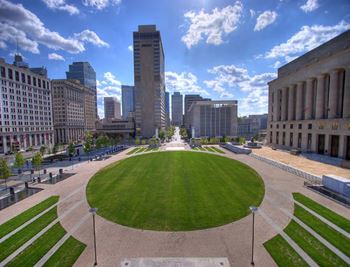 A large green field in the middle of a city with buildings in the background.