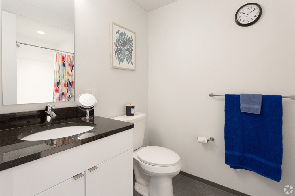 a bathroom with a sink toilet and mirror and a clock