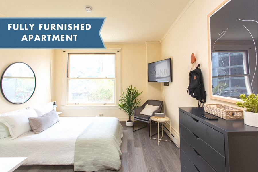 A fully furnished apartment with a bed, chair, and TV.