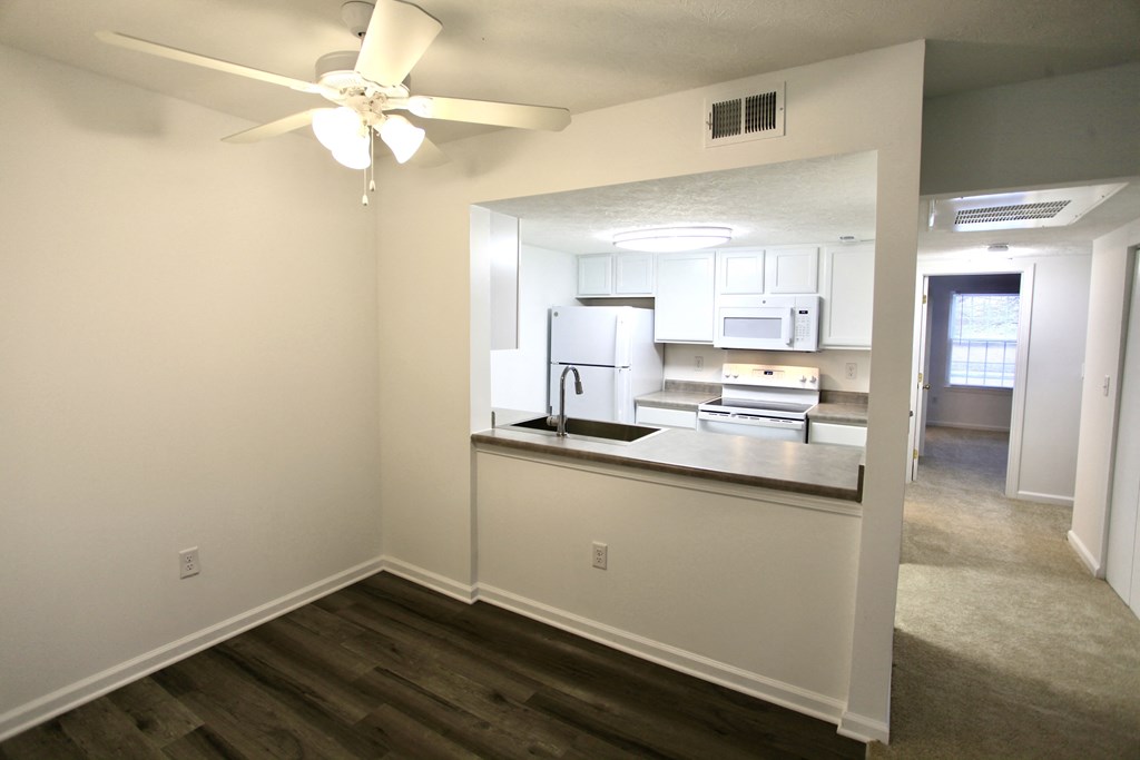 an empty living room with a kitchen and a ceiling fan