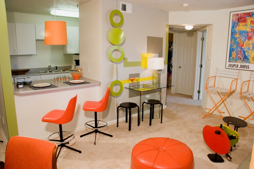 a living room and kitchen with orange chairs and a glass table