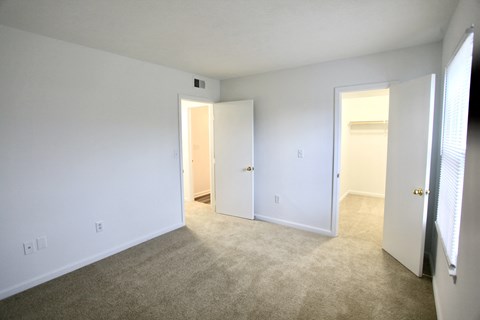 a bedroom with white walls and carpet and a door to a closet