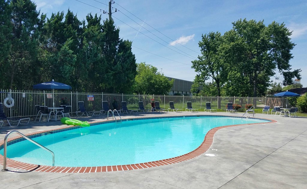 a resort style pool with chairs and umbrellas next to a fence