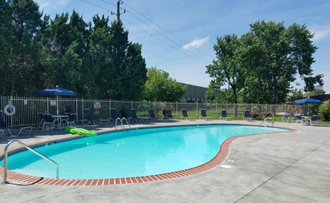 a resort style pool with chairs and umbrellas next to a fence