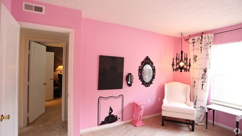 a pink and white bedroom with a chair and a mirror