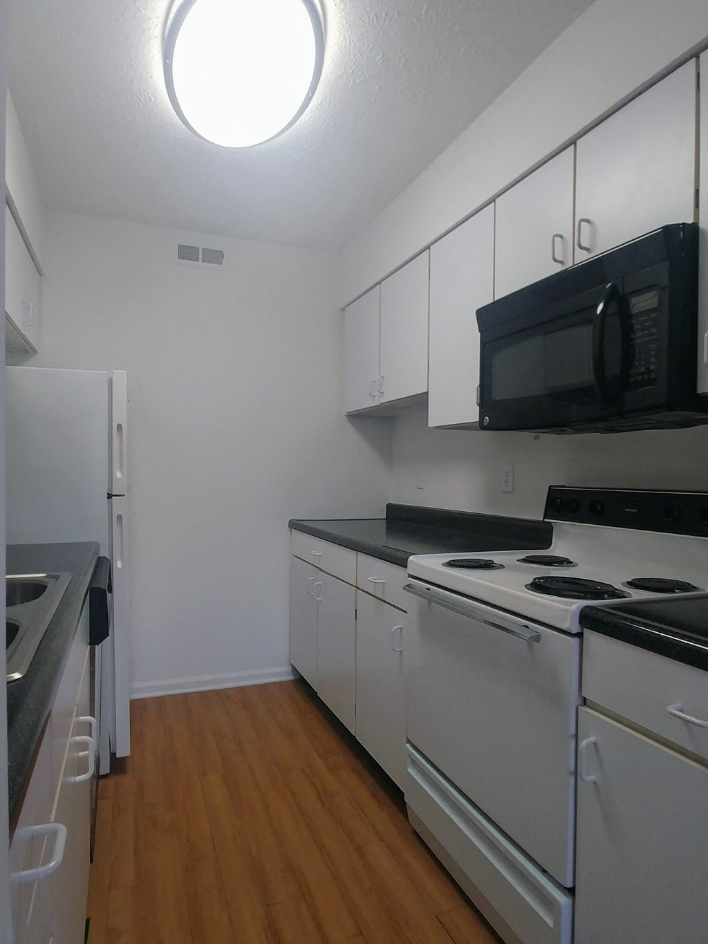 an empty kitchen with white appliances and a black microwave