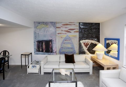 a living room with white furniture and a large painting on the wall