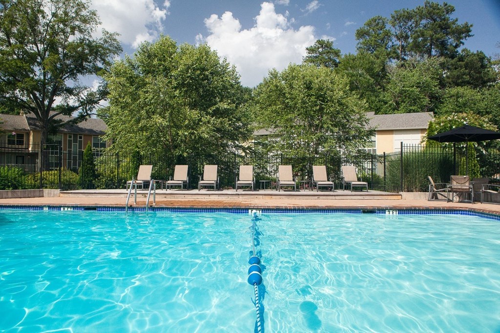 a swimming pool with chairs and trees in the background