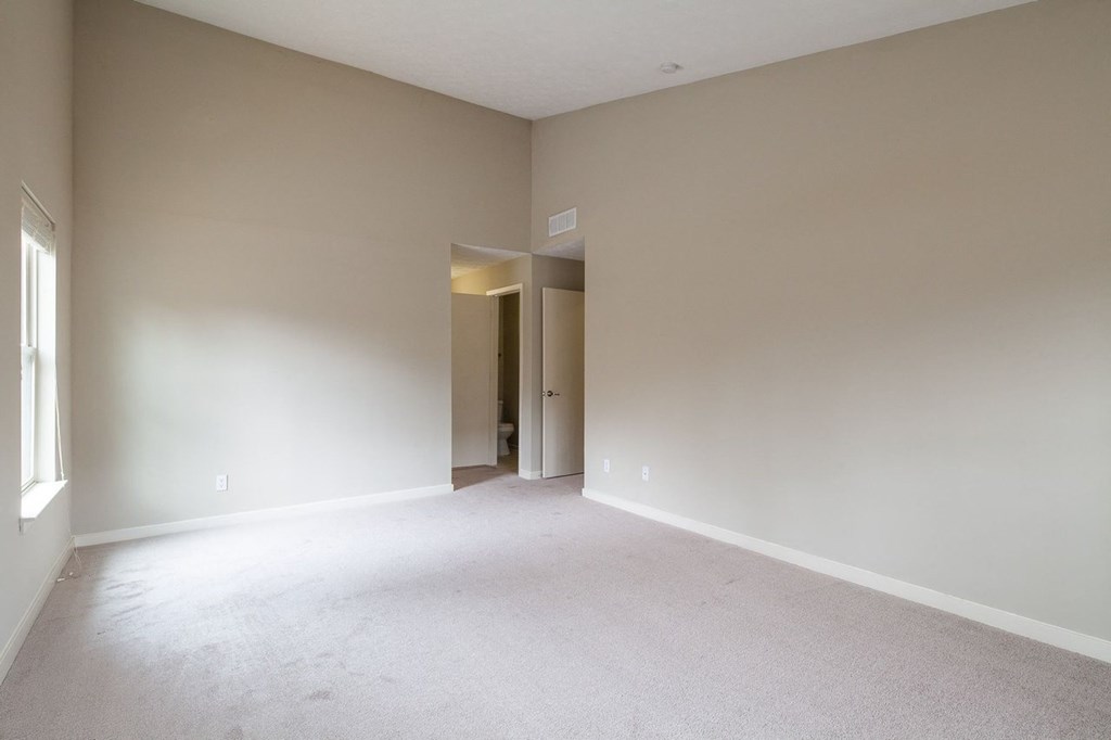 an empty living room with white carpet and a door to a hallway