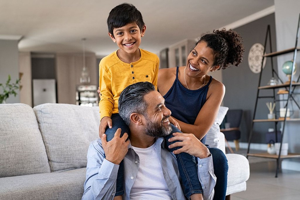 A family of three is sitting on a couch in a living room.