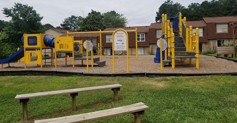 A playground with a yellow and blue slide, a yellow and blue climbing frame, and a yellow and blue swing set.