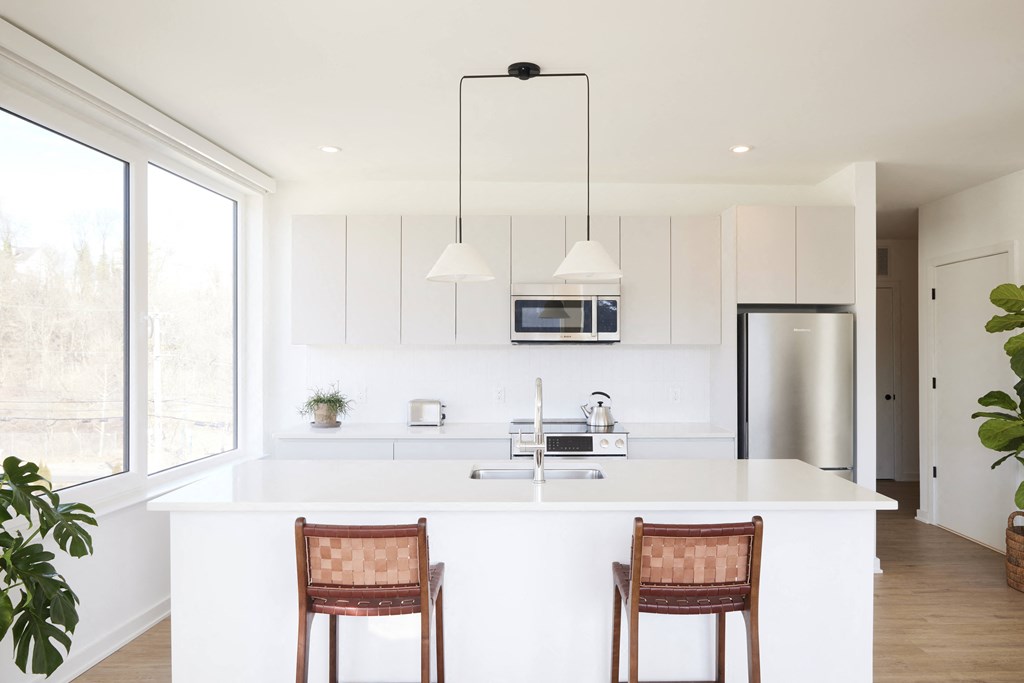 a kitchen with white cabinets and a white island with two chairs
