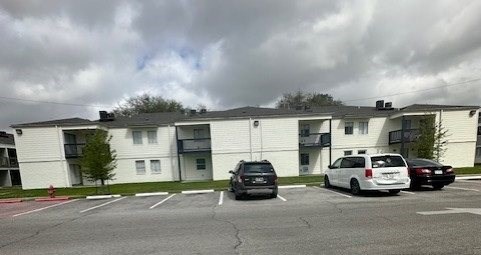 A parking lot in front of a white apartment building with cars parked.