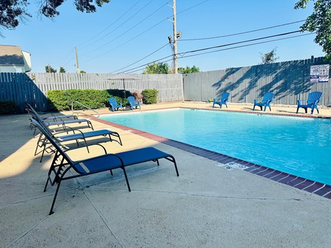 A pool with blue chairs and a fence in the background.
