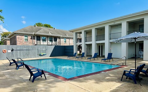 A pool surrounded by chairs and an umbrella in front of a building.