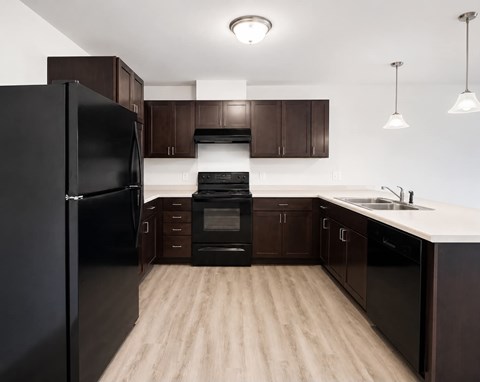 A black refrigerator stands in a kitchen with wooden floors and brown cabinets.