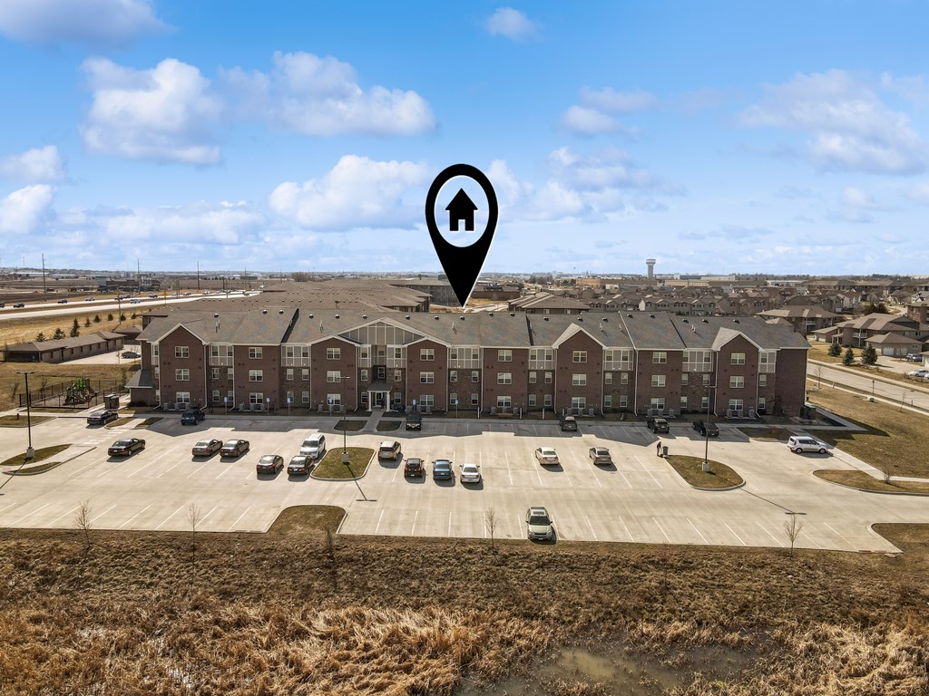 A large building with a parking lot in front and a sign with a house icon on it.
