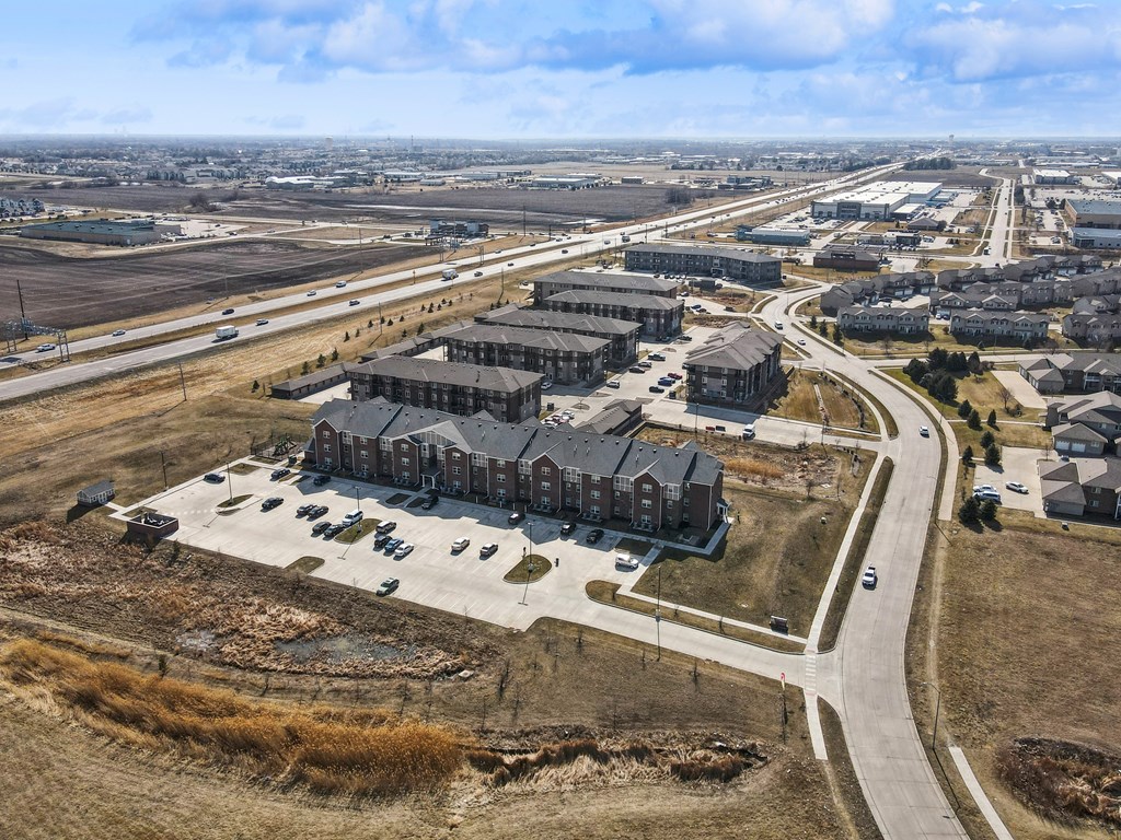 A large building complex with a parking lot in front is surrounded by a road.
