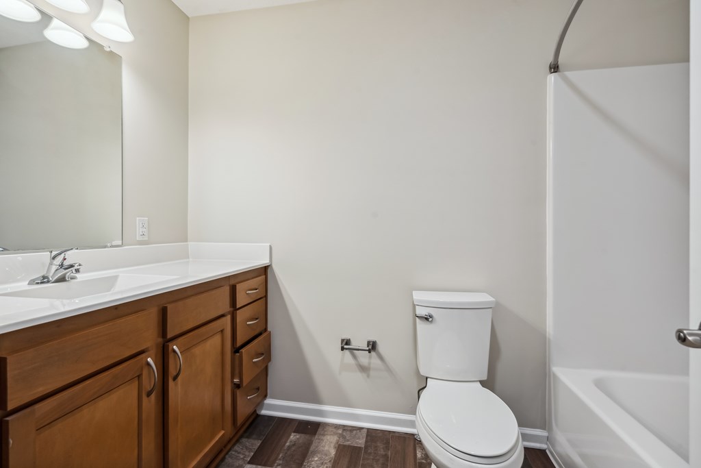 A white toilet sits in a bathroom next to a sink and a bathtub.