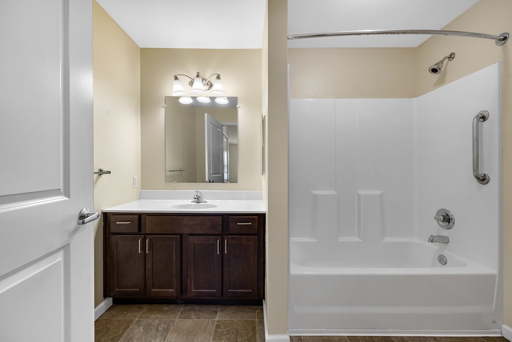 A white door is open to a bathroom with a white tub and brown cabinets.
